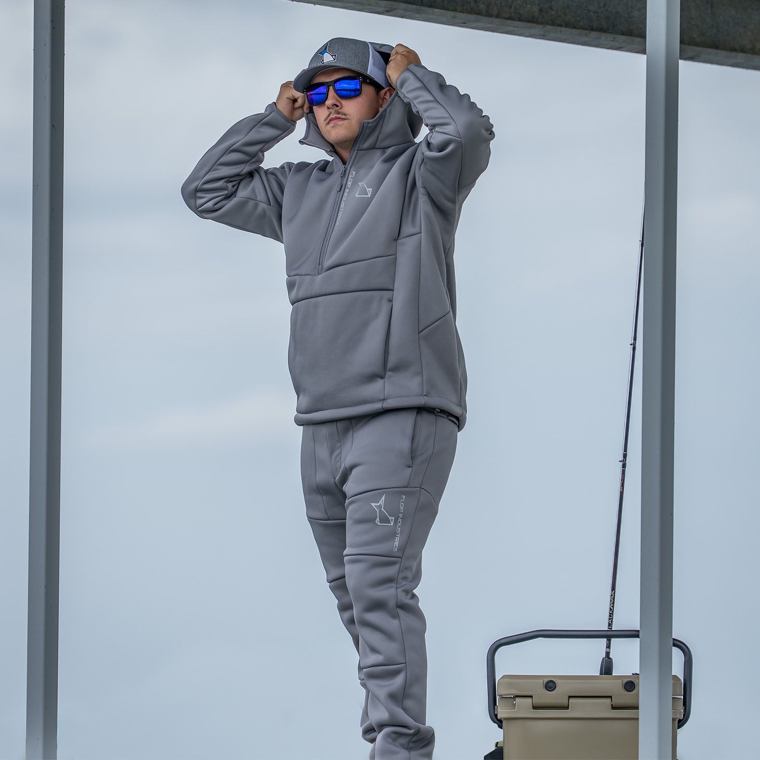 Person wearing a gray fleece jacket with a logo, standing outdoors against a light blue sky.